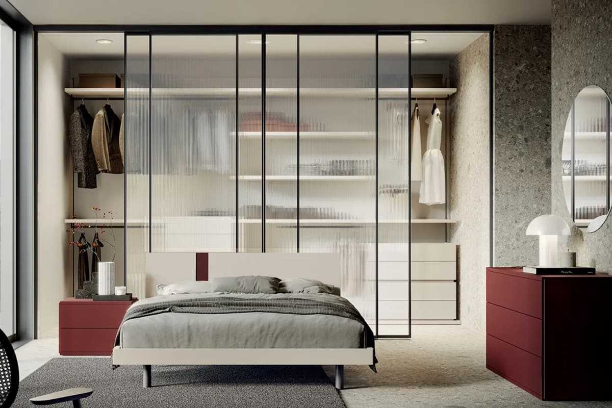Camera matrimoniale con cabina armadio con ante in vetro dietro al letto